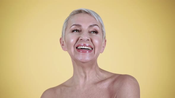 Mature woman with bare shoulders laughing against yellow background