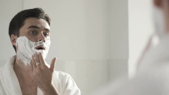 Closeup Reflection in Mirror of Confident Handsome Young Man Applying Shaving Foam