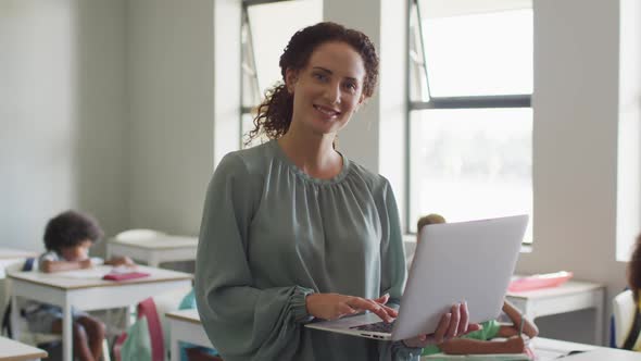 Video of happy caucasian female teacher using laptop at school during lessons