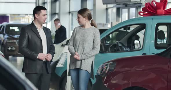 Cheerful Caucasian Young Woman Taking Car Keys From Dealer, Clapping Hands and Showing Victory