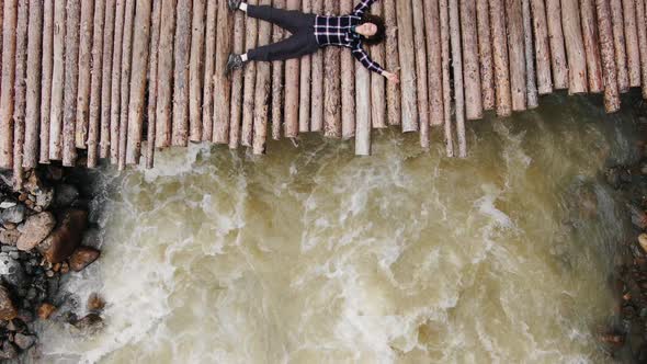 Young Woman Lies on Wooden Footbridge Over Rough River