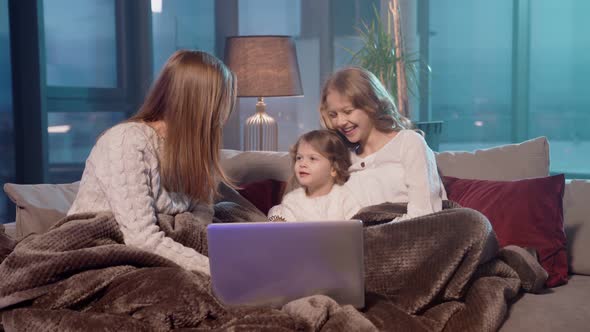 Two Sisters Resting with Mother on Couch and Using Laptop