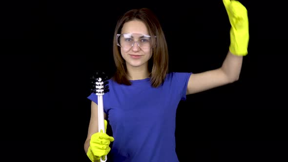 A Young Woman Is Reaching a Toilet with a Toilet Brush and Showing Biceps. Woman in Safety Glasses