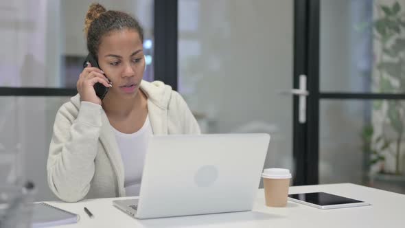 African Woman Talking on Smartphone While Using Laptop in Office