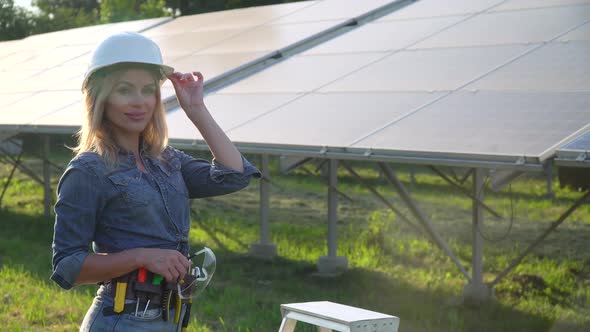 Female Engineer in a White Helmet Is at the Solar Power Station. The Green Energy Concept alt