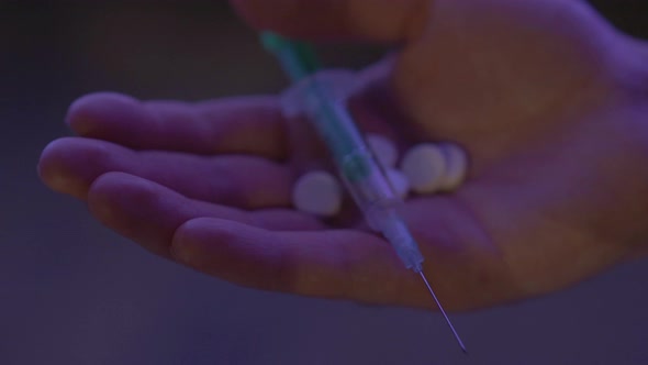 Close-up of Male Caucasian Hand with Pills and Syringe in Neon Lights. Unrecognizable Drug Dealer