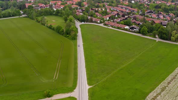 Camera downswing of a drone which follows a car coming out of a town driving down a road at springti