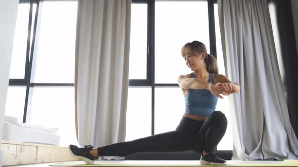 Attractive Japanese Woman Doing Yoga in Her Living Room with a Large Window in the Background