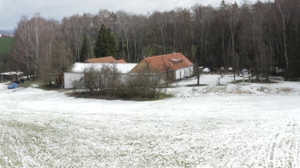 Farmhouse with snowy fields and leafless trees in winter countryside.