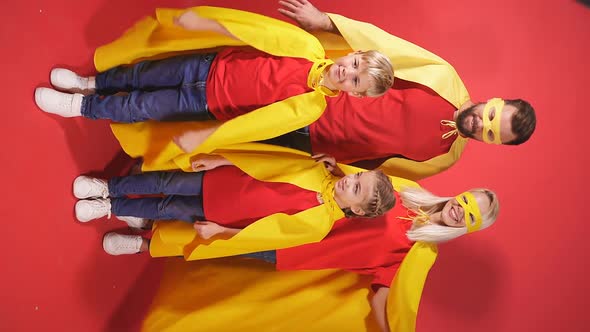 Family of Superheroes in Costumes Posing in Studio with Red Background