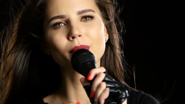 Girl in a Microphone Sings Driving Songs and Smiles. Black Background. Close Up