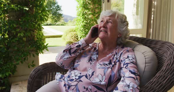 Caucasian senior woman talking on smartphone while sitting on the chair outdoors