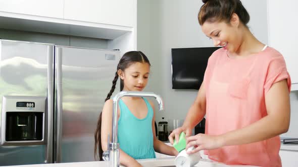 Mother teaching daughter to washing crockery in kitchen