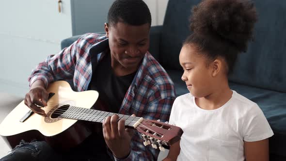 AfricanAmerican Man Teaching His Little Son to Play Guitar at Home