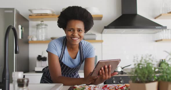 Portrait of happy african american woman preparing dinner using tablet in kitchen