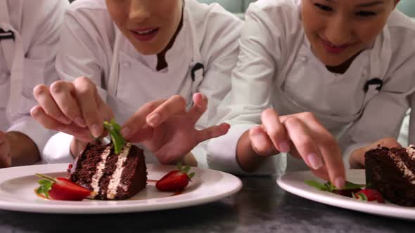 Line of Chefs Garnishing Dessert Plates with Mint Leaves and Strawberries