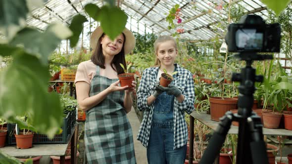 Mother and Daughter Vloggers Recording Video in Greenhouse Waving Hand Talking Showing Thumbsup