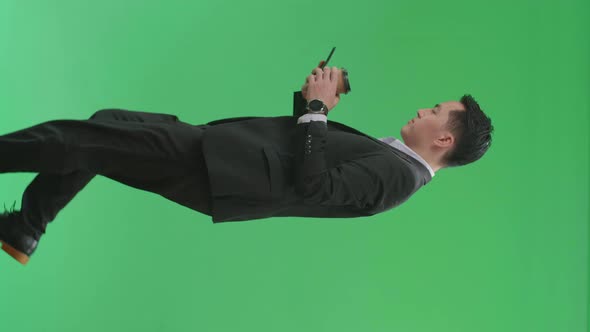 Side View Of Asian Business Man Use Mobile Phone And Drink Coffee While Walking On Green Screen