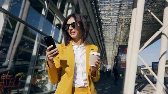 young professional businesswoman in a classic suit uses a smartphone and drink coffee
