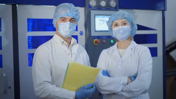 Man and Woman in Uniform and Masks Stand Near New Equipment