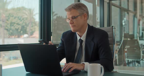 A businessman ending a phone call while working on a laptop at the office