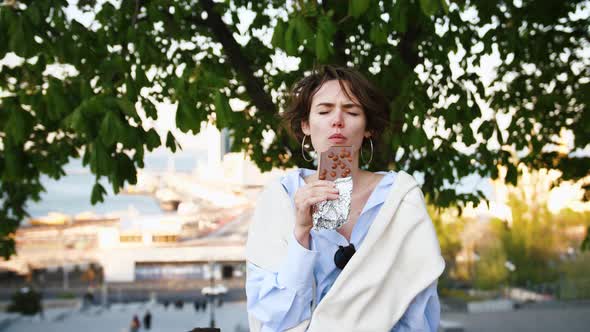 Portrait of a Beautiful Stylish Hipster Girl Tasting Chocolate Outdoors in City Park