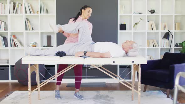 Video of happy biracial female physiotherapist exercising with caucasian senior man