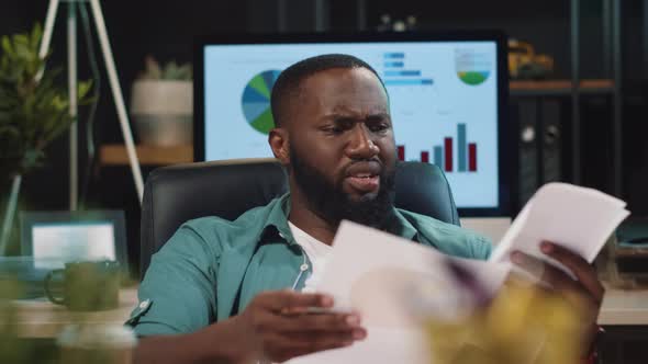 Closeup Disappointed African Hipster Guy Looking at Diagrams in Night Office