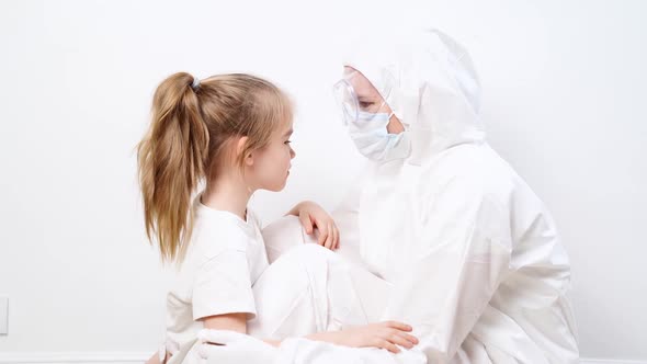 A Little Girl Hugs a Doctor in a White Protective Suit Mask Glasses and Gloves