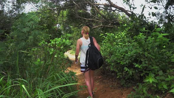 traveler girl with a backpack walking along a trail on a tropical island, watching forest