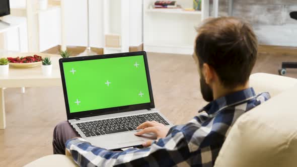 Man Sitting on the Sofa with a Green Screen Laptop in His Lap