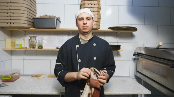 Portait of Young Cook in Uniform Standing at Kitchen Restaurant and Wiping His Hands with a Towel