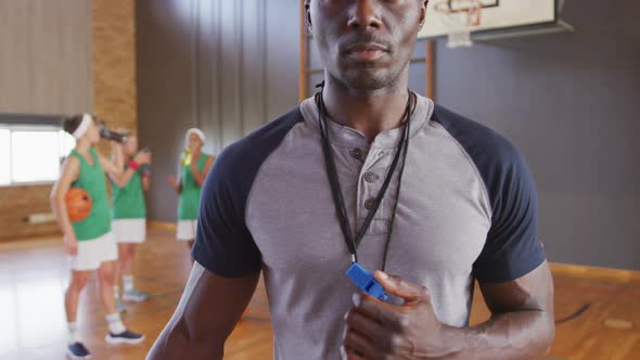 Portrait of african american male coach with diverse female basketball team in background