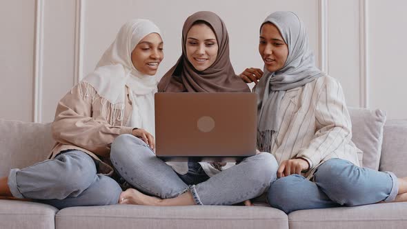 Three Muslim Girls Look at the Laptop Smile and Laugh in Bright Beige Studio