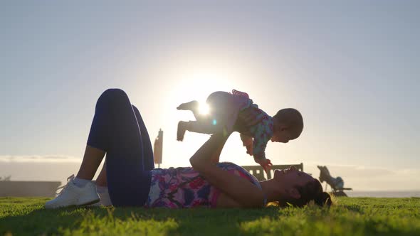 Young Mother Is Keeping on Her Arms and Playing with a Baby Girl on a Ocean Beach at Sunset