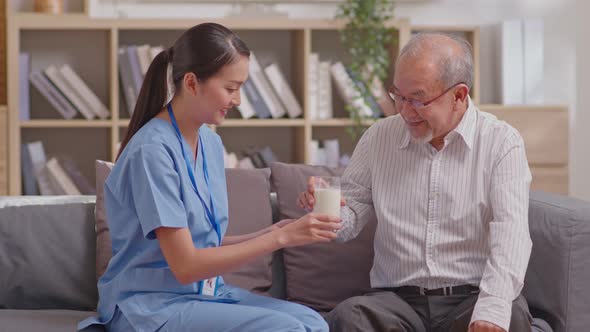 Asian beautiful therapist doctor serve milk to older patient in nursing home. Asian nurse in uniform