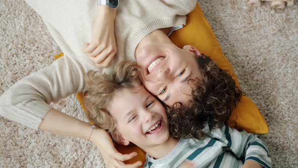 Top View of Young Lady and Little Boy Laughing and Looking at Camera Lying on Floor Together