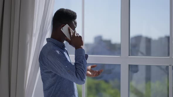 Young Businessman Talking on the Phone Looking Out the Window in Home Office