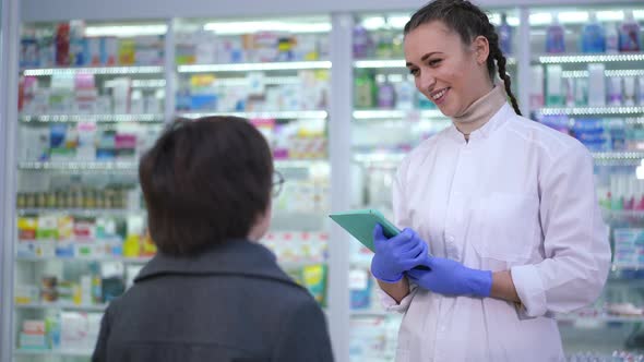 Young Positive Pharmacist Talking with Boy Standing in Drugstore Indoors