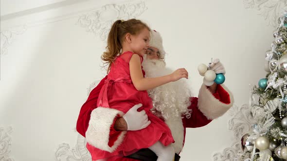 Santa Claus Helping Little Girl To Hang Baubles on Top of the Christmas Tree