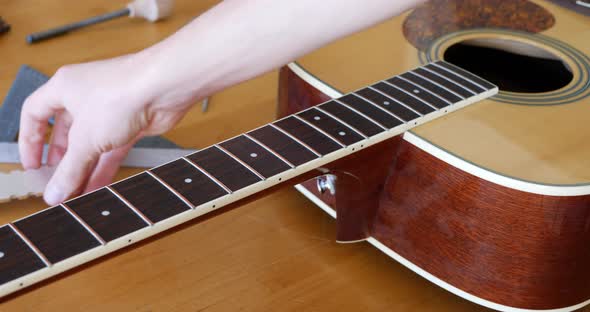 Close up hands of a luthier measuring, sanding and leveling the frets on an acoustic guitar neck on
