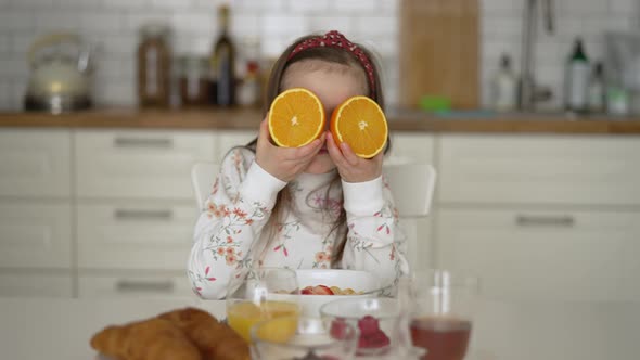 Little Girl with Fresh Orange Having Fun During Breakfast