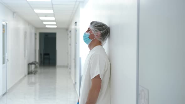 Side View Devastated Doctor Sliding Down the Wall in Hospital Hallway Indoors