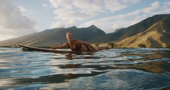 Beautiful woman paddling out to surf at sunset alt
