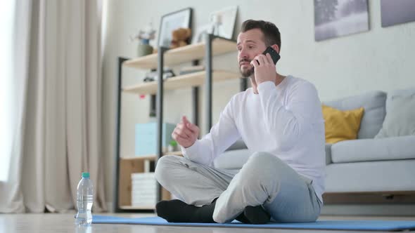 Man Talking on Smartphone on Yoga Mat at Home