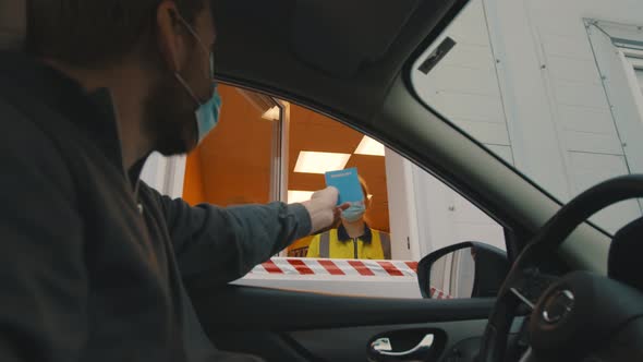 Man in Car Wearing Safety Mask Giving Passport To Customs Officer in Booth