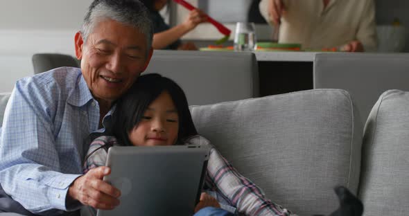 Front view of cute asian granddaughter and old senior grandfather using digital tablet at home 4k