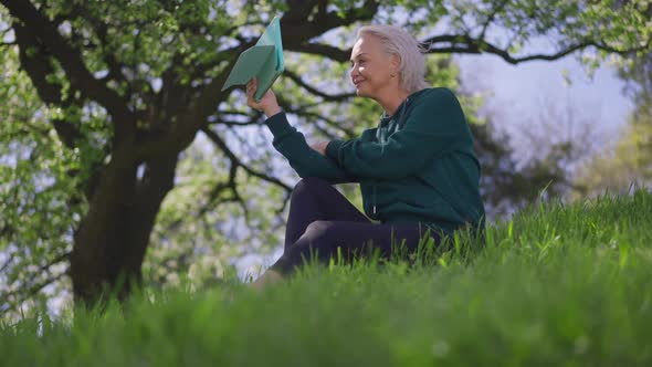 Happy Relaxed Senior Woman Talking at Tablet Video Chat Smiling Sitting on Green Spring Summer