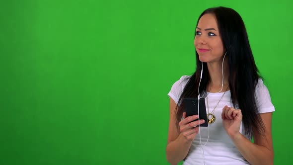 Young Pretty Woman Listens Music with Earphone on Smartphone - Green Screen - Studio