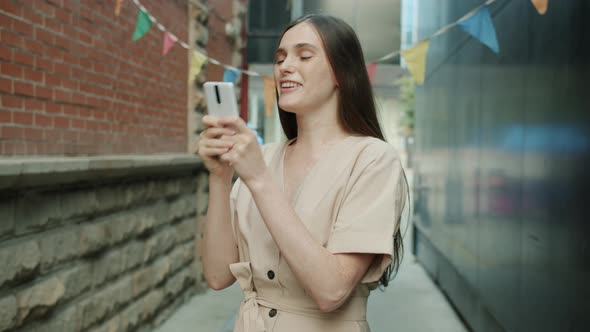 Portrait of Joyful Woman Getting Great News in Smart Phone Message Laughing Holding Device Outdoors